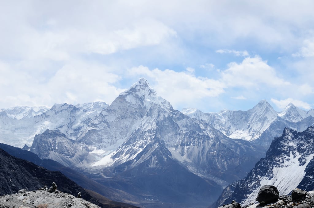 Snow-capped mountains rise majestically against a cloudy sky, showcasing a range of jagged peaks and expansive valleys. The landscape is marked by rocky outcrops and patches of snow, contributing to a serene and rugged natural beauty.
