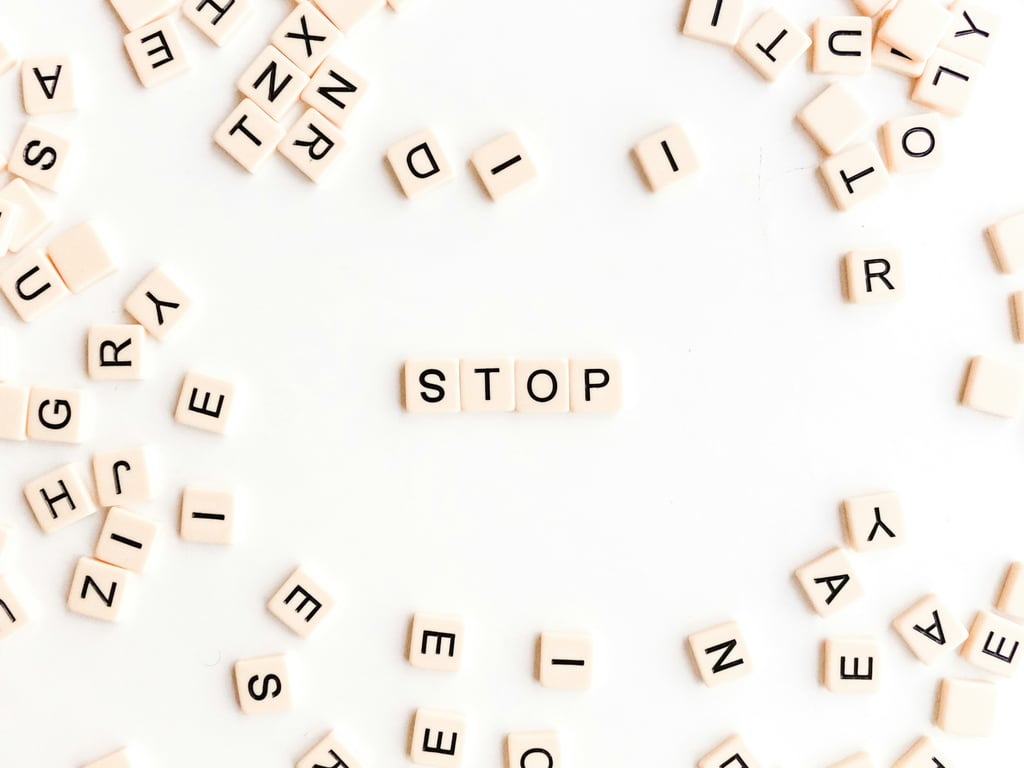 Wooden Scrabble letter tiles scattered on a white background with the word "STOP" spelled out in the center. The individual tiles display various letters including S, T, O, P, R, E, A, N, D, and others arranged randomly around the formed word.